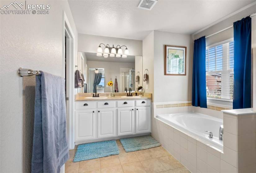 Bathroom with a textured ceiling, vanity, tile floors, and tiled bath