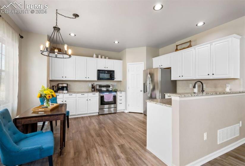 Kitchen with pendant lighting, appliances with stainless steel finishes, light hardwood / wood-style flooring, and white cabinets