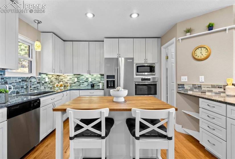 Kitchen featuring decorative light fixtures, appliances with stainless steel finishes, tasteful backsplash, dark stone counters, and light wood-type flooring