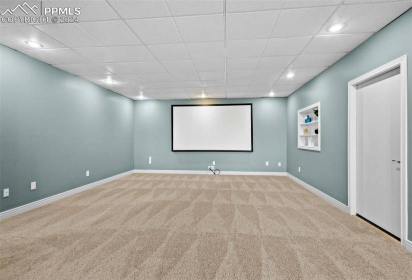 Home theater with a drop ceiling, light colored carpet, and built in features