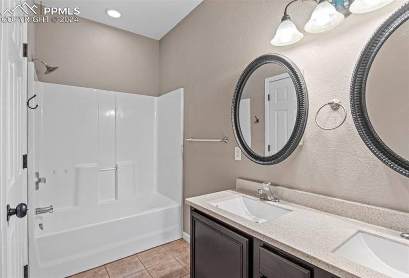 Bathroom featuring shower / washtub combination, double sink, tile flooring, and vanity with extensive cabinet space