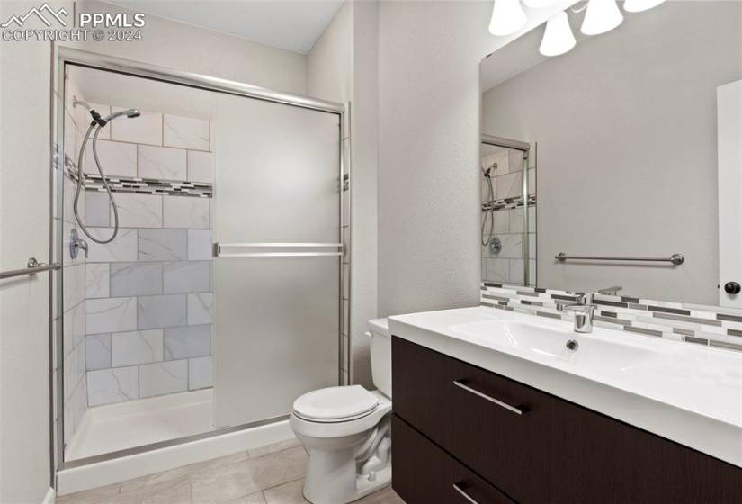 Bathroom with tile floors, backsplash, a shower with shower door, oversized vanity, and toilet
