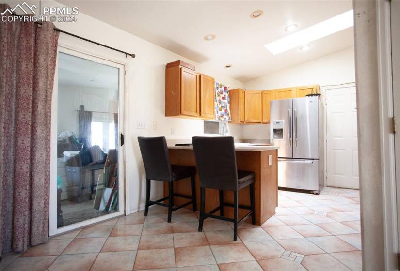Kitchen featuring kitchen peninsula, vaulted ceiling, stainless steel refrigerator with ice dispenser, a breakfast bar, and light tile floors