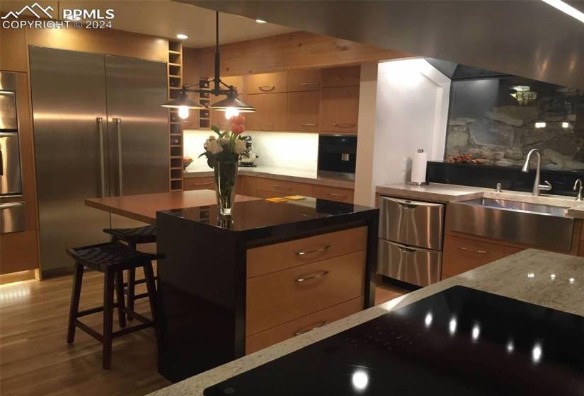 Kitchen with appliances with stainless steel finishes, a kitchen island, dark wood-type flooring, dark stone countertops, and pendant lighting