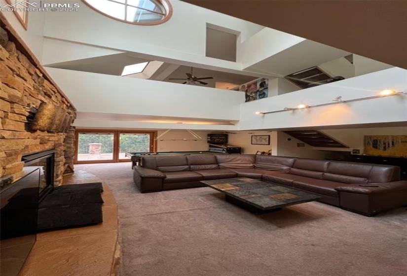 Living room with light carpet, a high ceiling, ceiling fan, and a stone fireplace