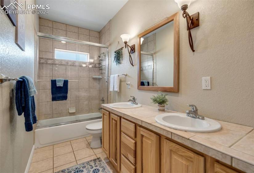 Full Main bathroom with tile flooring, shower / bath combination with glass door, and double sink vanity