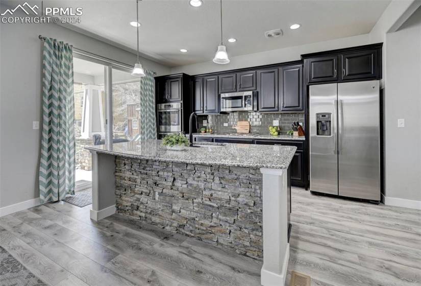 Kitchen with appliances with stainless steel finishes, backsplash, light wood-type flooring, decorative light fixtures, and light stone countertops