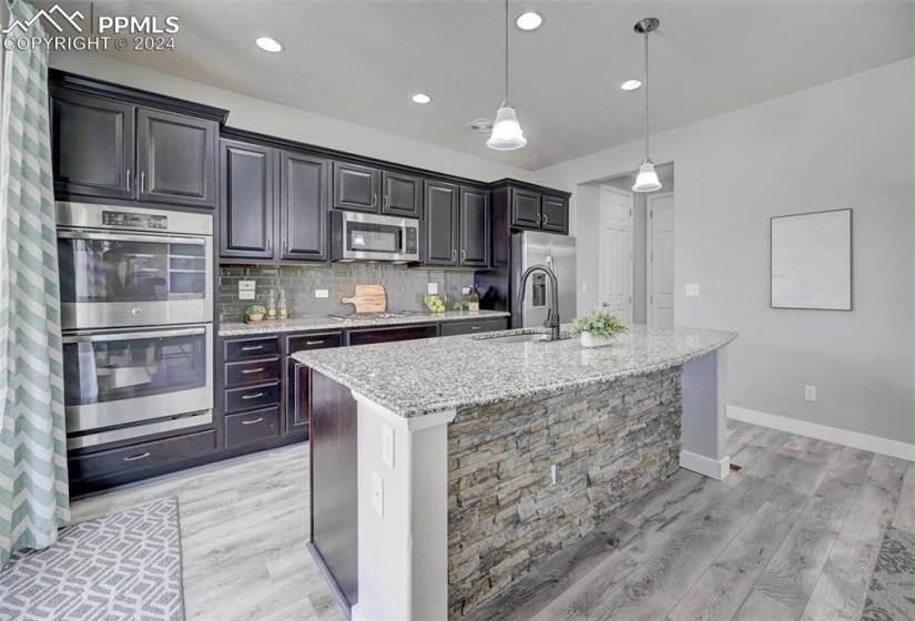 Kitchen with stainless steel appliances, tasteful backsplash, a kitchen island with sink, pendant lighting, and light wood-type flooring