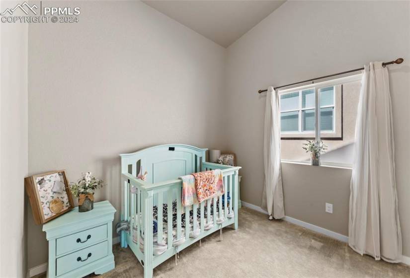 Bedroom featuring light colored carpet, vaulted ceiling, and a nursery area