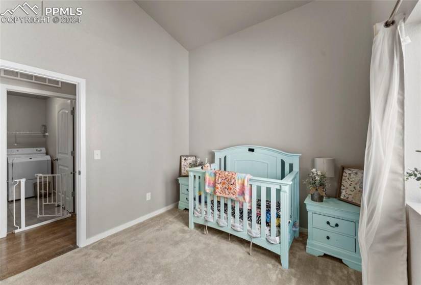 Bedroom featuring light hardwood / wood-style flooring, a crib, vaulted ceiling, and washer / dryer