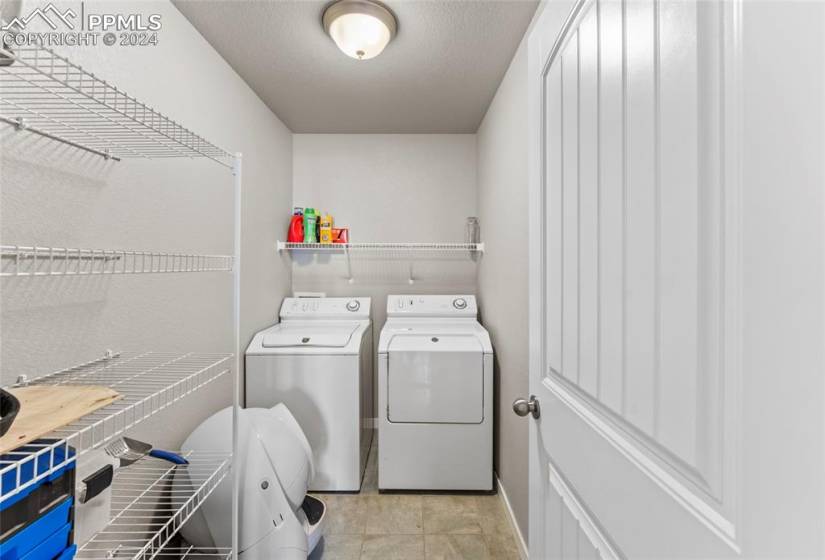 Clothes washing area featuring washing machine and clothes dryer and light tile flooring