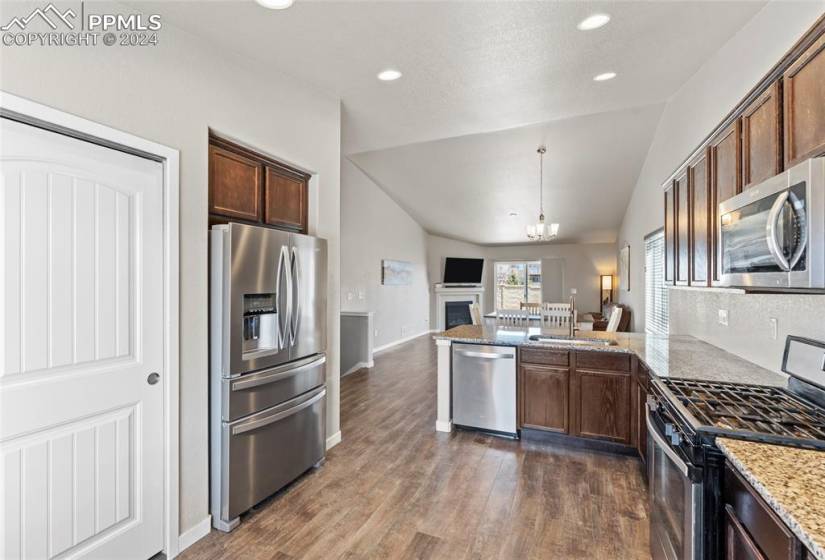 Kitchen featuring appliances with stainless steel finishes, dark wood-type flooring, vaulted ceiling, and light stone counters