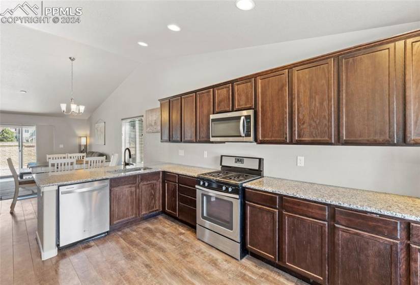Kitchen with light wood-type flooring, kitchen peninsula, appliances with stainless steel finishes, sink, and vaulted ceiling