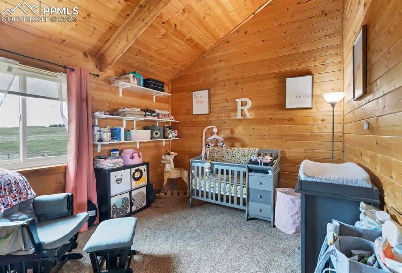Bedroom with lofted ceiling with beams, light carpet, wooden walls, wood ceiling, and a nursery area