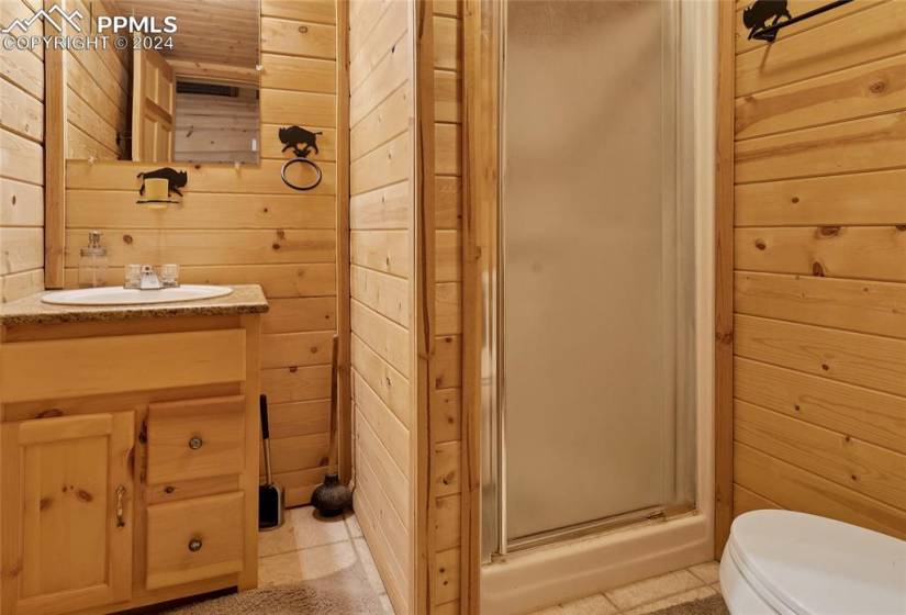 Bathroom featuring tile flooring, walk in shower, vanity, and wooden walls