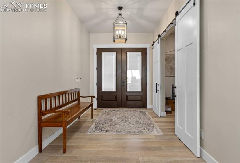 Foyer entrance featuring french doors, an inviting chandelier, light wood-type flooring, and a barn door