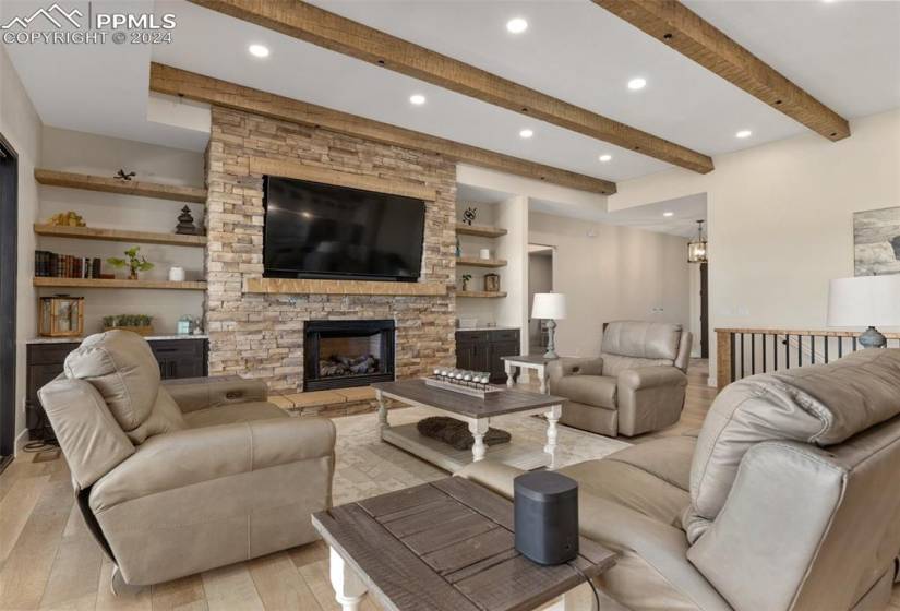 Living room featuring a stone fireplace, built in features, beamed ceiling, and light wood-type flooring