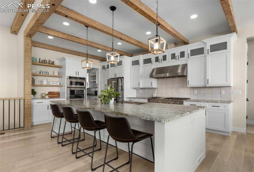 Kitchen with beamed ceiling, an island with sink, stainless steel appliances, and pendant lighting