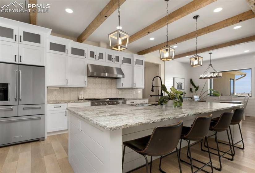 Kitchen with hanging light fixtures, high end fridge, and a kitchen island with sink
