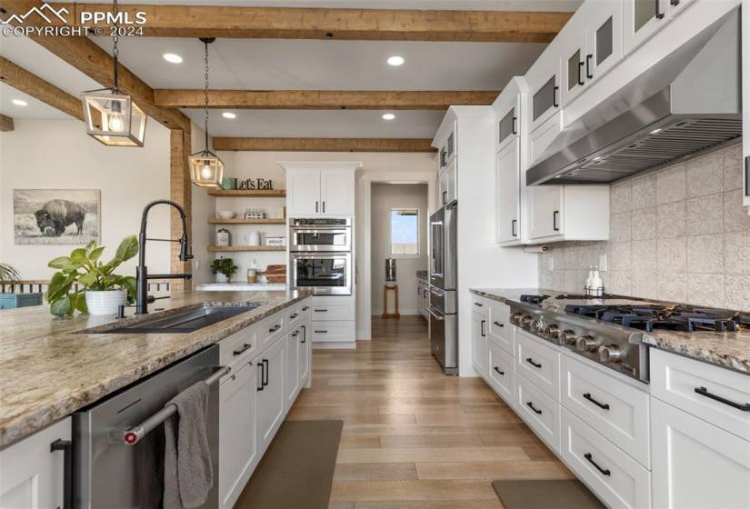 Kitchen with light wood-style floors, backsplash, white cabinetry, decorative light fixtures, and stainless steel appliances