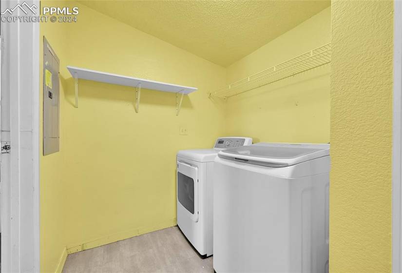 Clothes washing area with washing machine and clothes dryer, a textured ceiling, and light hardwood / wood-style floors