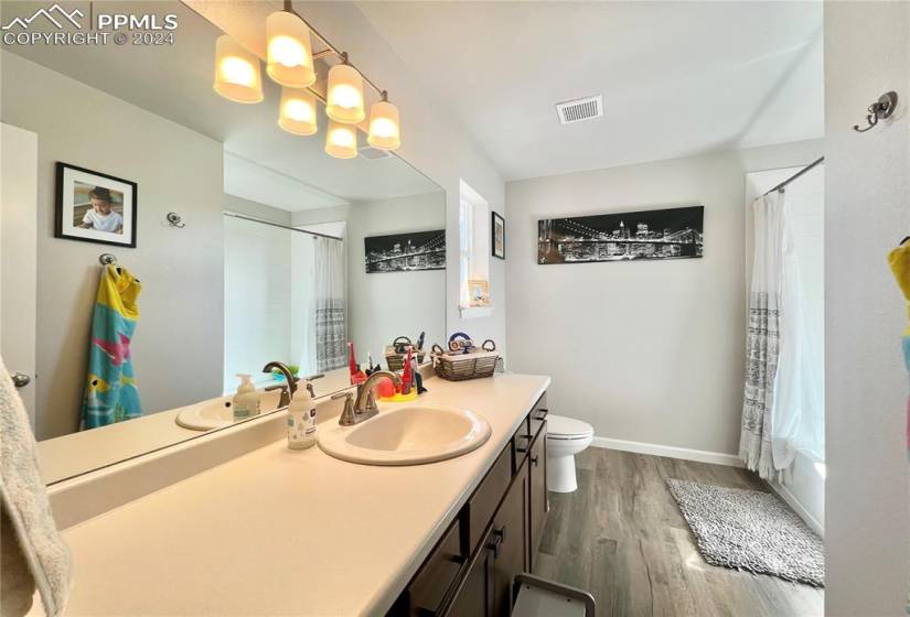 Bathroom featuring hardwood / wood-style floors, a notable chandelier, vanity with extensive cabinet space, and toilet
