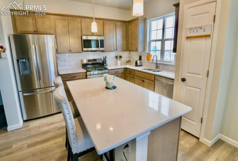 Kitchen with appliances with stainless steel finishes, light hardwood / wood-style flooring, hanging light fixtures, sink, and a center island