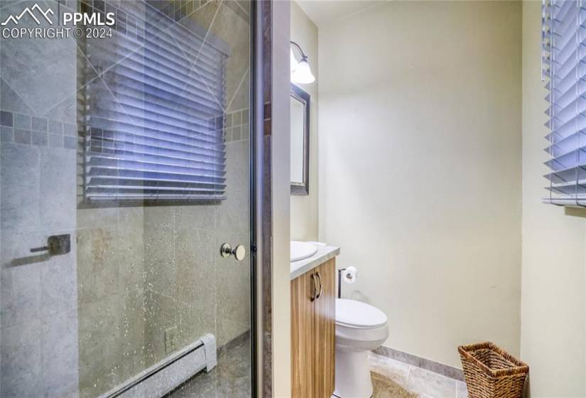 Bathroom featuring a baseboard radiator, vanity, a shower with shower door, tile flooring, and toilet