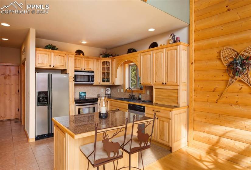 Kitchen with sink, appliances with stainless steel finishes, backsplash, tile flooring, and a kitchen island breakfast bar