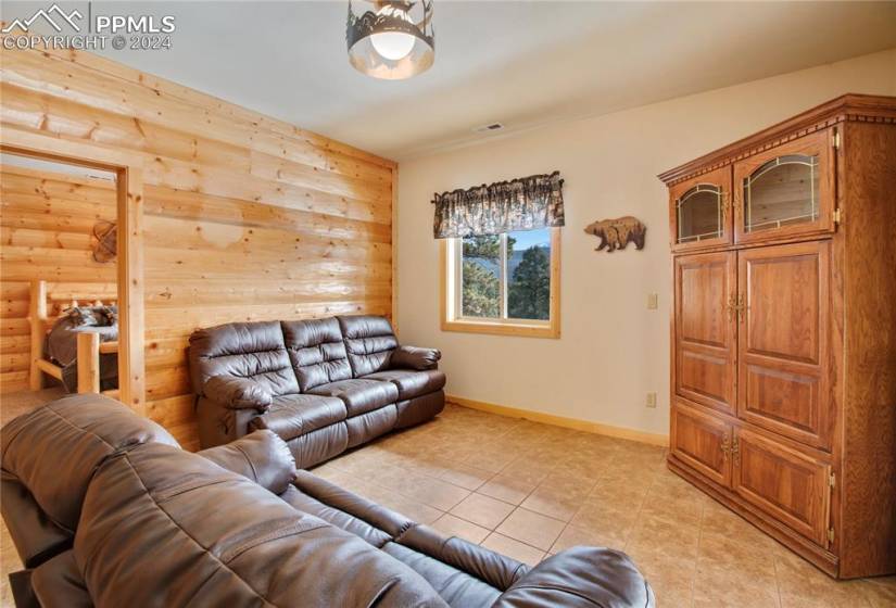 Lower level family room with tile floors and log walls, includes a gas line for a future corner freestanding stove.