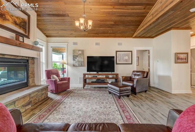 Living room featuring a stone fireplace, wooden ceiling, hardwood / wood-style flooring, and an inviting chandelier