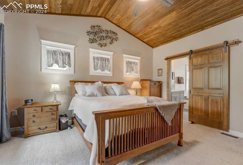 Bedroom with light colored carpet, ensuite bath, a barn door, and wooden ceiling