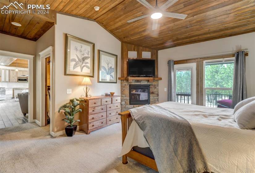 Bedroom featuring a stone fireplace, ceiling fan, access to outside, wood ceiling, and carpet floors