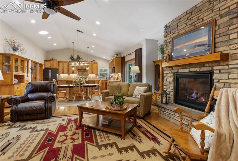 Family room with ceiling fan, hardwood floor, vaulted ceiling, and a stone gas fireplace