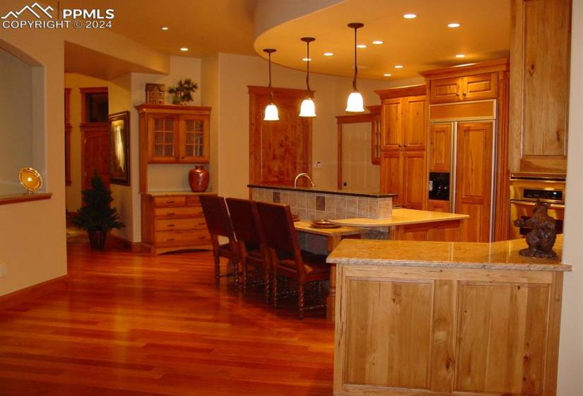 Kitchen featuring stainless steel oven, dark hardwood / wood-style floors, paneled built in fridge, decorative light fixtures, and light stone countertops