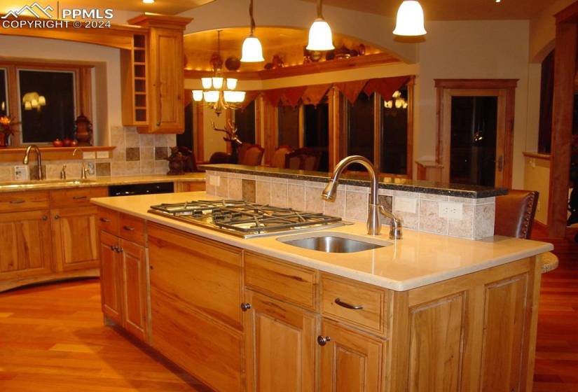 Kitchen with backsplash, an island with sink, hanging light fixtures, and light hardwood / wood-style flooring