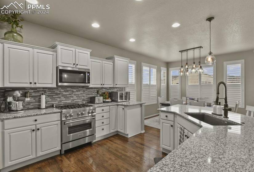 Kitchen with pendant lighting, dark hardwood / wood-style flooring, stainless steel appliances, and white cabinets