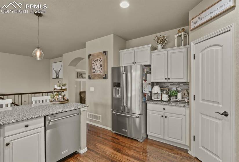 Kitchen with white cabinets, dark wood-type flooring, appliances with stainless steel finishes, and decorative light fixtures