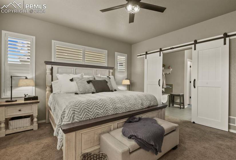 Primary bedroom featuring a barn door and ceiling fan