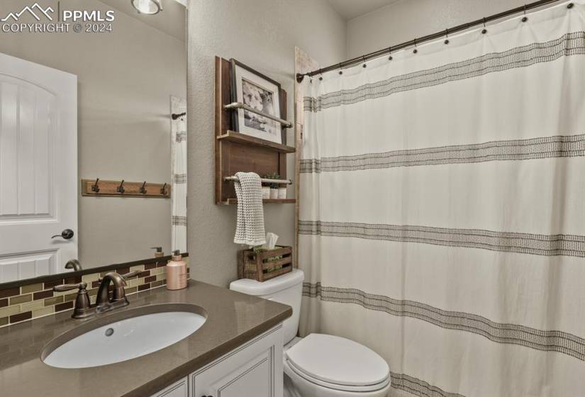 Main level guest bathroom featuring backsplash, toilet, and vanity with extensive cabinet space