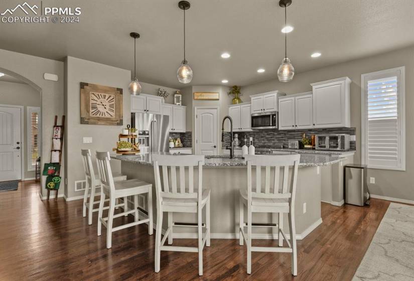 Kitchen featuring appliances with stainless steel finishes, backsplash, white cabinetry, dark hardwood / wood-style flooring, and pendant lighting