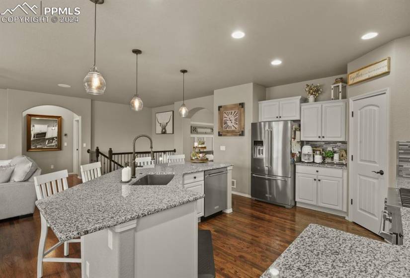 Kitchen with hanging light fixtures, light stone counters, stainless steel appliances, and white cabinetry