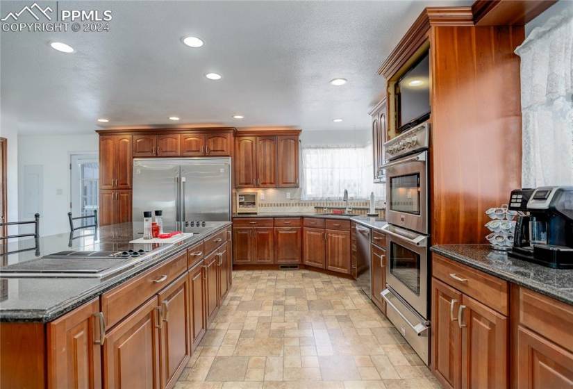 Kitchen with backsplash, appliances with stainless steel finishes, light tile floors, sink, and dark stone counters