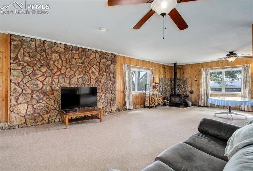 Carpeted living room featuring wood walls, ceiling fan, and a wood stove