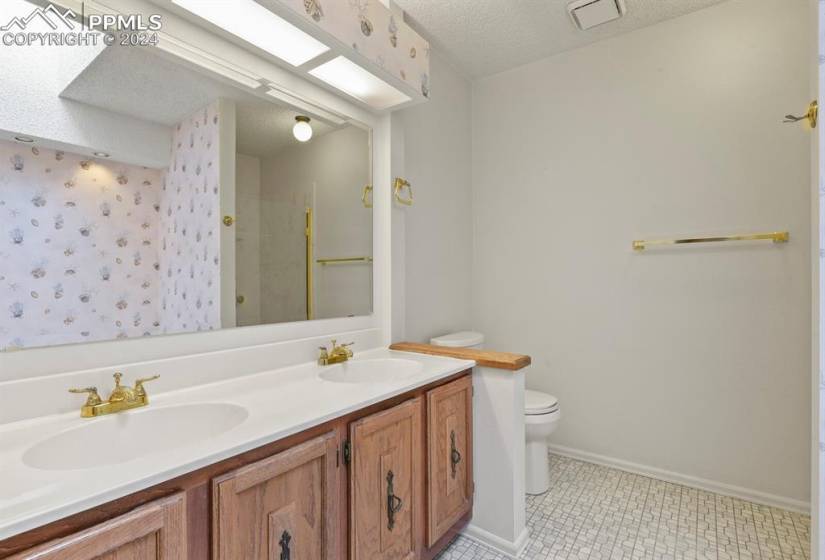 Bathroom with vanity with extensive cabinet space, toilet, tile flooring, a textured ceiling, and dual sinks