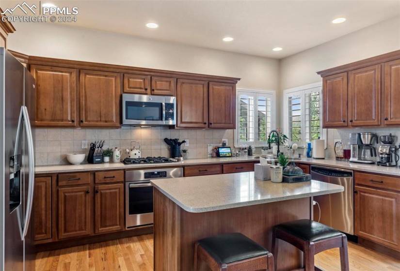 Kitchen featuring appliances with stainless steel finishes, a kitchen island, light hardwood / wood-style floors, backsplash, and a kitchen breakfast bar