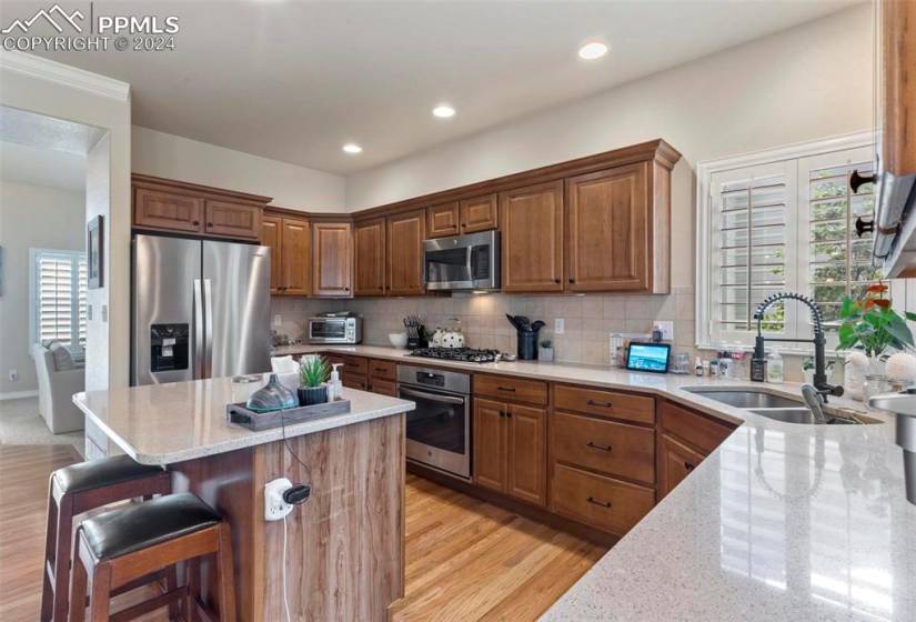 Kitchen with backsplash, stainless steel appliances, sink, light wood-type flooring, and a breakfast bar