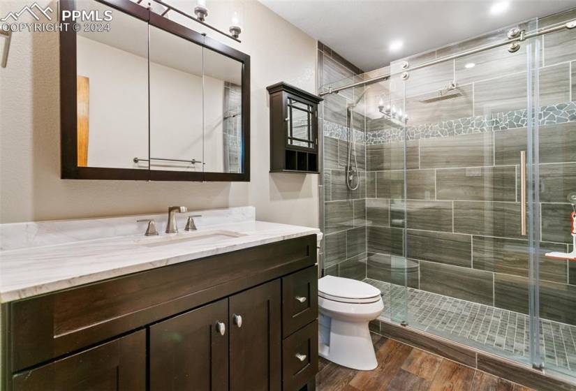 Bathroom featuring vanity with extensive cabinet space, wood-type flooring, toilet, and walk in shower