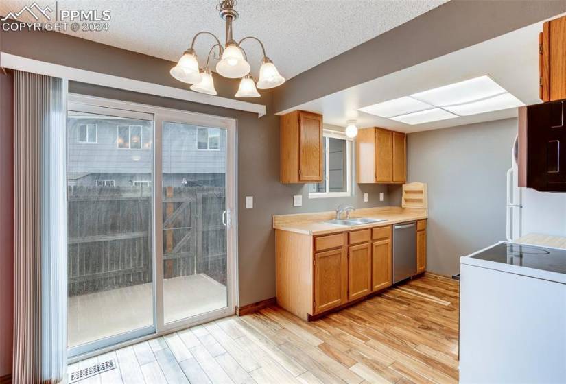 Kitchen with decorative light fixtures, light hardwood / wood-style flooring, a notable chandelier, sink, and dishwasher