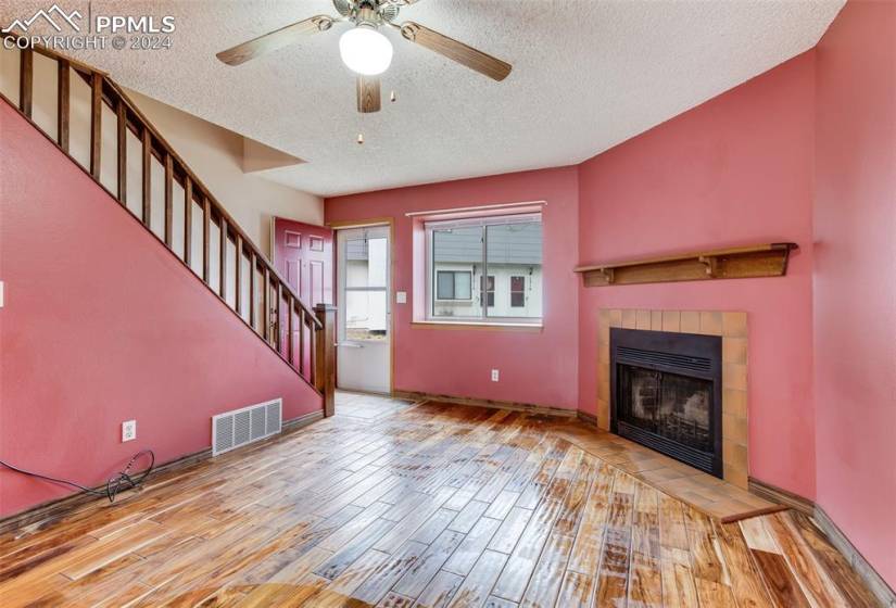 Unfurnished living room featuring wood-type flooring, a textured ceiling, ceiling fan, and a tile fireplace